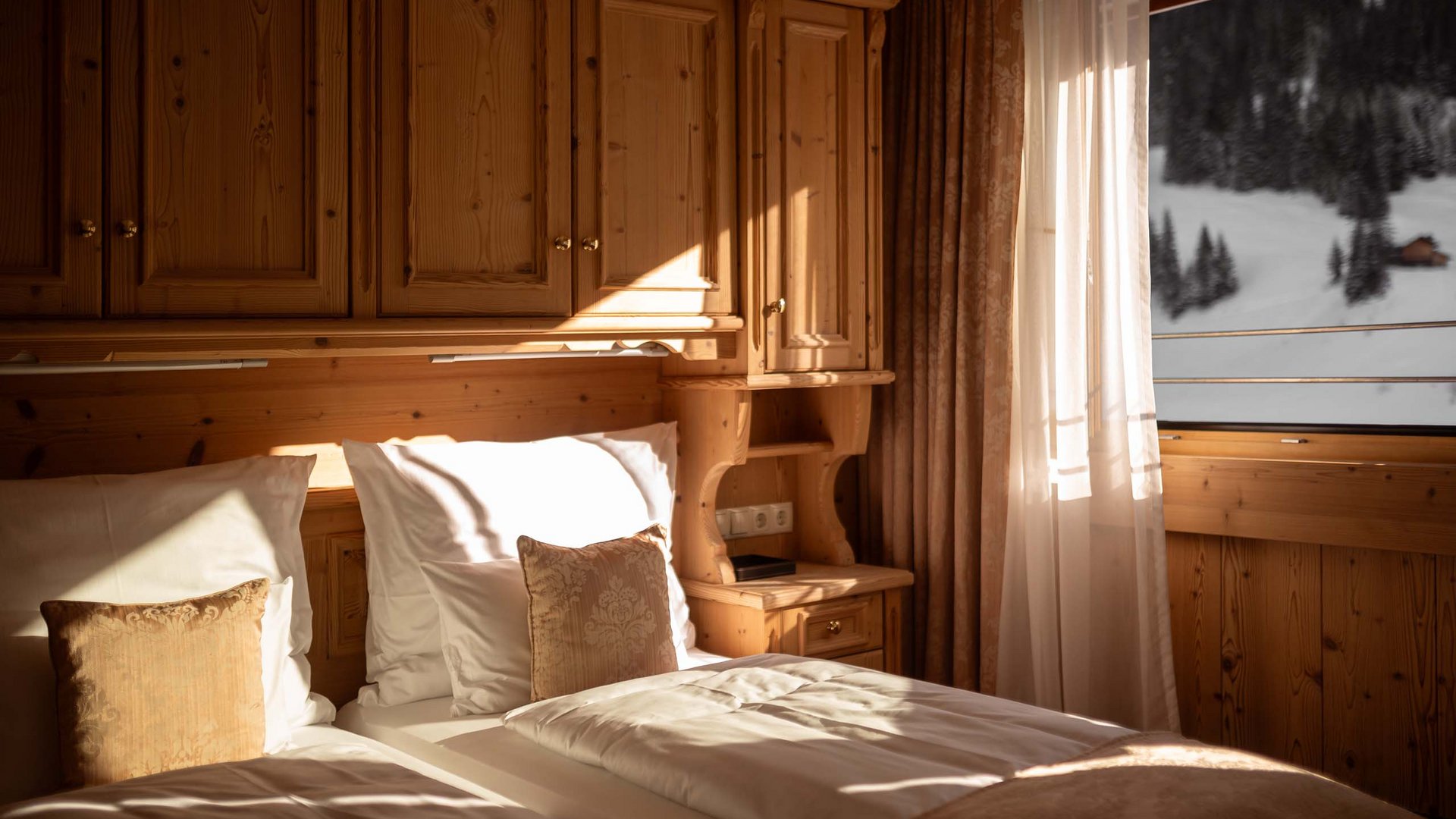 Das Verwall | Your accommodation in Lech am Arlberg Cozy bedroom with two beds and wooden furniture in warm sunlight