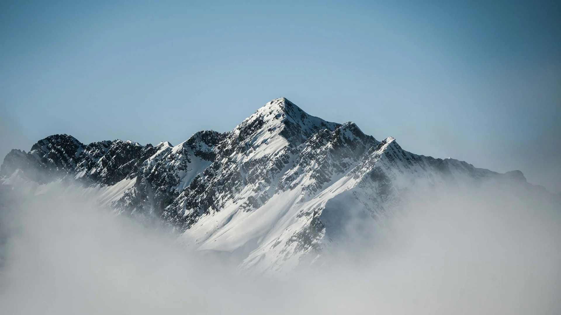 Schneebedeckter Berggipfel ragt über Nebel hervor unter klarem Himmel