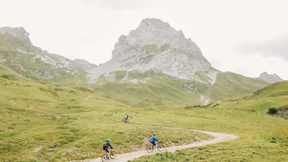 Drei Radfahrer auf einem Bergweg vor einer großen Felsformation
