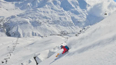 Skifahrer fährt steil den schneebedeckten Berg hinunter mit Alpen im Hintergrund