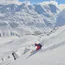 Skifahrer fährt steil den schneebedeckten Berg hinunter mit Alpen im Hintergrund