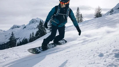Snowboarder fährt einen schneebedeckten Berg hinab mit Bergen im Hintergrund
