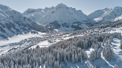 Schneebedecktes Alpendorf mit hohen Kiefern und Berggipfeln