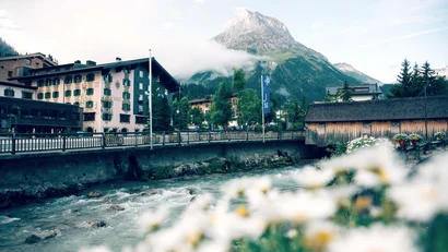 Blick auf ein Dorf mit Berg, Fluss und unscharfen Blumen im Vordergrund