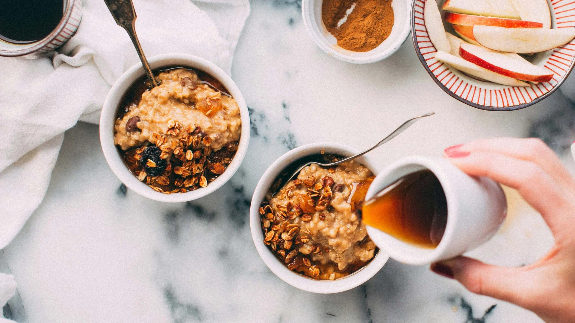 Schüsseln mit Haferbrei, Granola, Obst und Kaffee auf Marmoroberfläche