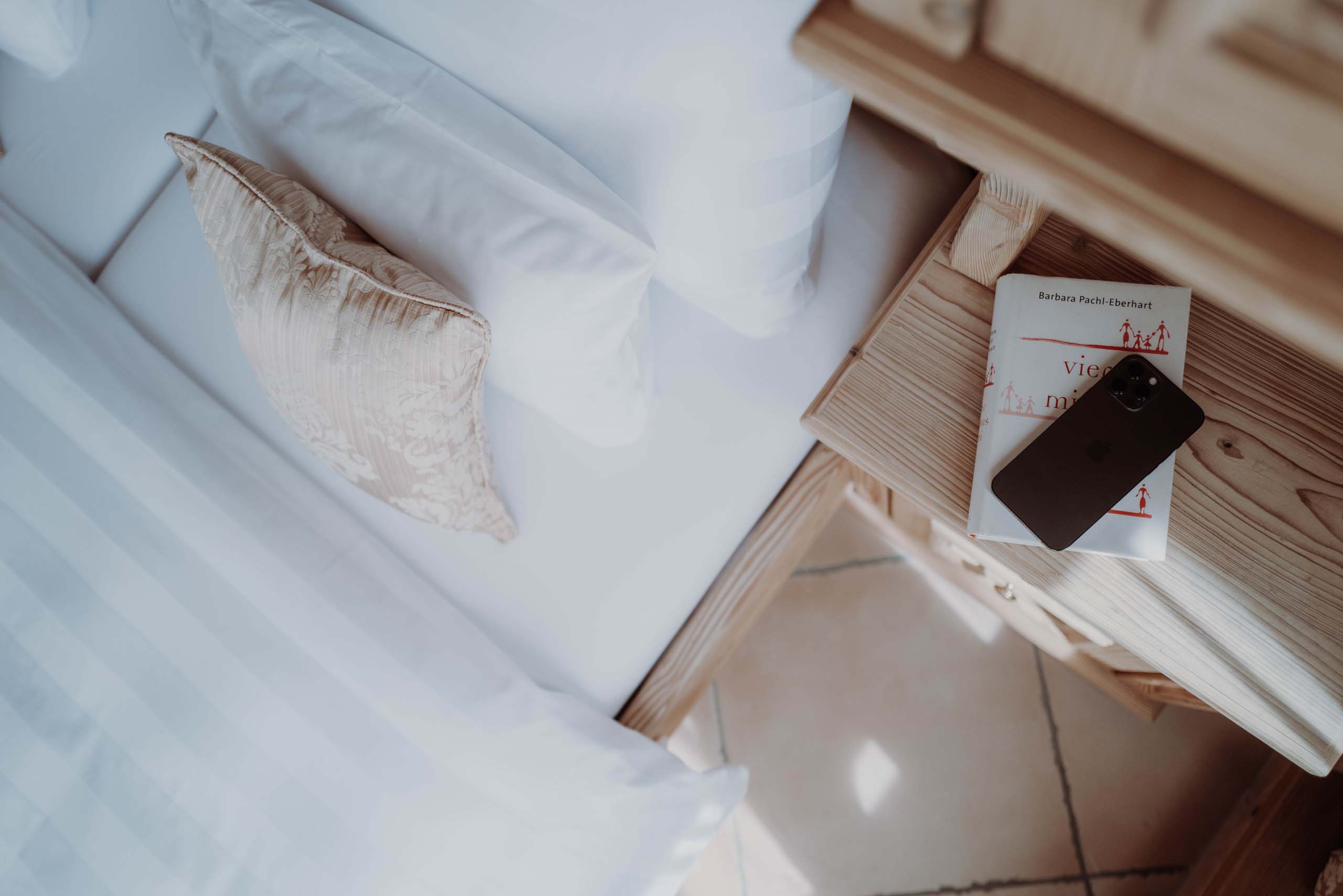 Bett mit Kissen und Nachttisch mit Buch und Smartphone